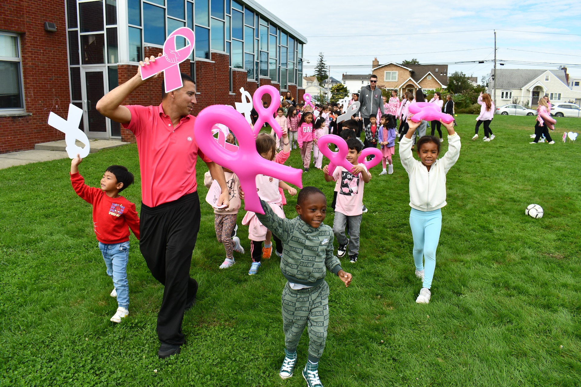 Students and a teacher wave inflatable pink ribbons while walking on a grass field
